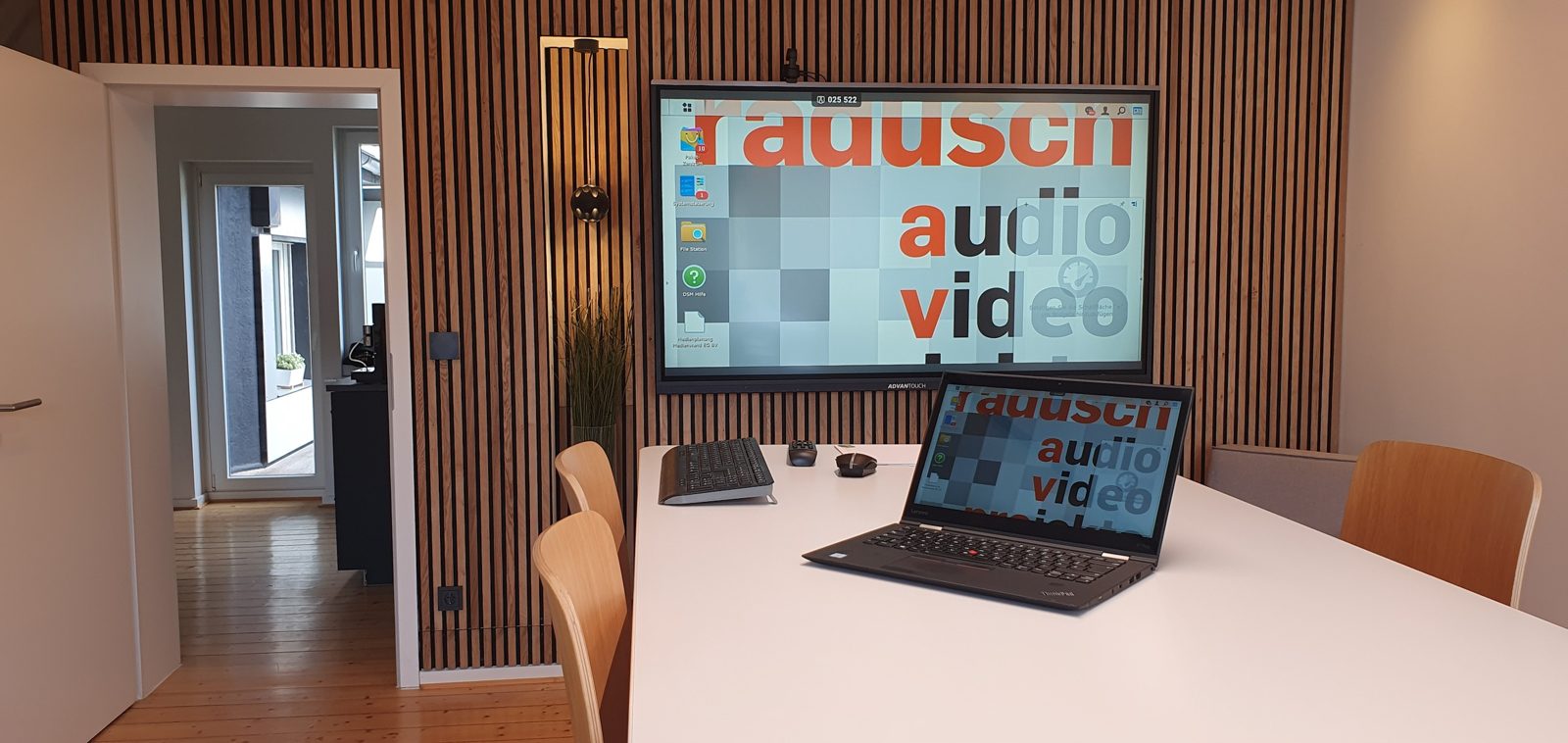 Besprechungsraum mit großem Bildschirm, Holzlamellenwand und Laptop auf dem Konferenztisch